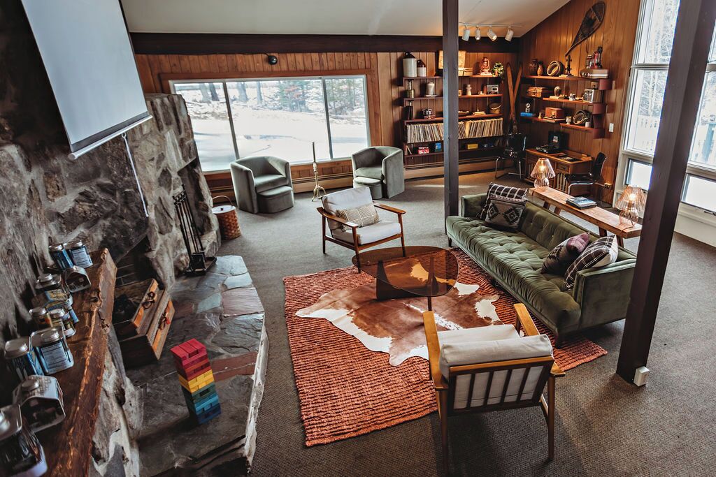 A cozy living room with a stone fireplace, leather sofa, and a bookshelf filled with books and decorative items.