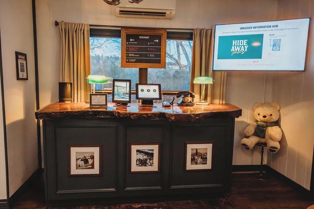 A reception desk with a monitor, framed pictures, a teddy bear, and a screen displaying 'HIDE AWAY'.