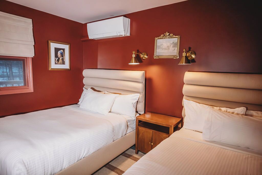 A hotel room with two beds, a nightstand, and wall-mounted lamps.