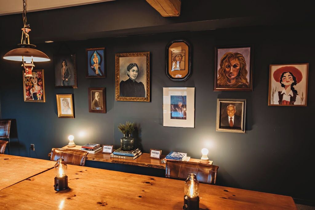 A room with a wooden table, framed portraits, and a dark wall.