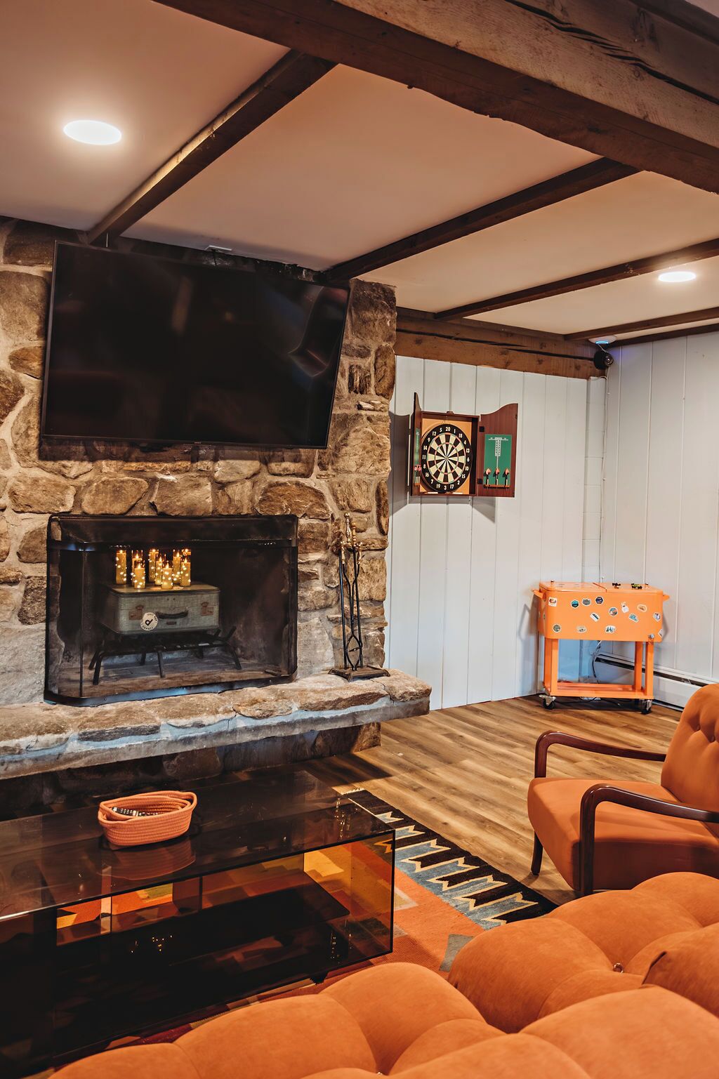 Un salon chaleureux avec une cheminée en pierre, un téléviseur à écran plat, un jeu de fléchettes et des meubles de couleur orange.