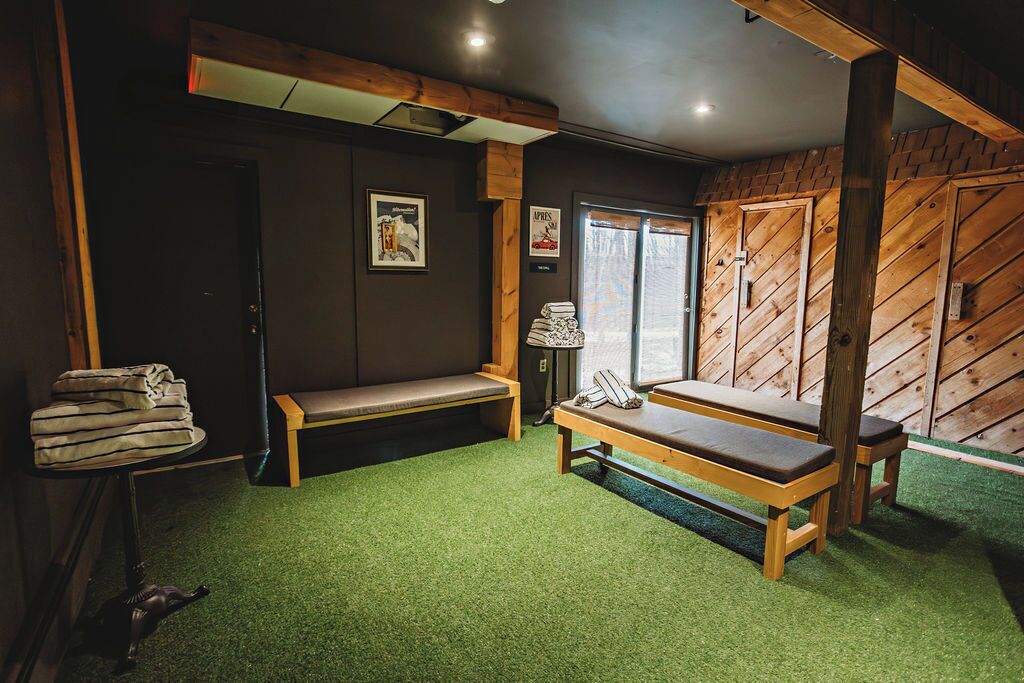 Um quarto com um banco de madeira, uma mesinha com toalhas, um banco com almofadas e uma janela com cortinas.