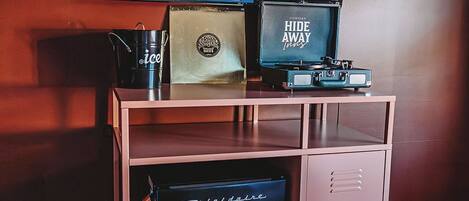 Una habitación compacta con un televisor montado en la pared, un refrigerador pequeño, una cafetera y un letrero que dice 'Hide Away'.