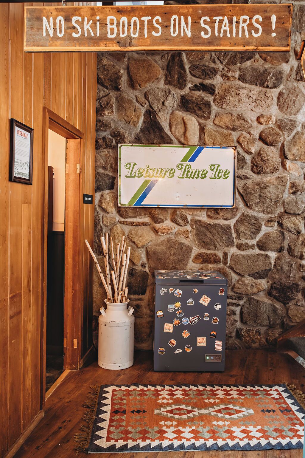 A wooden door with a sign reading "NO SKI BOOTS ON STAIRS!" and a sign for "Leisure Time Ice" above a stone wall.