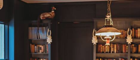 A wooden dining table with candle-like lights, surrounded by leather chairs, in a room with bookshelves and a door.