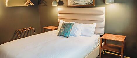 A neatly made bed with a headboard, two bedside tables, a wall-mounted air conditioner, and a painting above the bed.