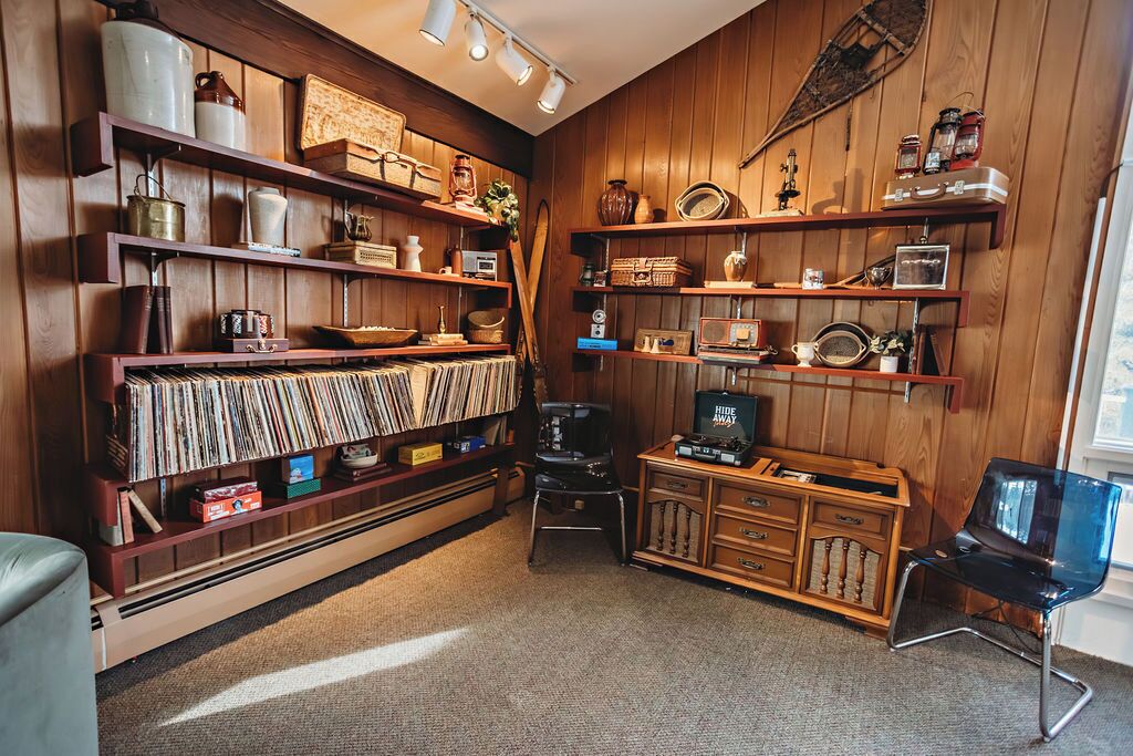 Une pièce avec des étagères en bois remplies de livres, d’objets décoratifs et de radios anciennes. On y trouve également un vieux juke-box et une petite armoire en bois dotée de tiroirs.