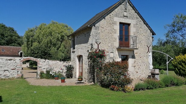 Une maison en pierre dotée d’un balcon, entourée d’un jardin bien entretenu et d’un mur en pierre.