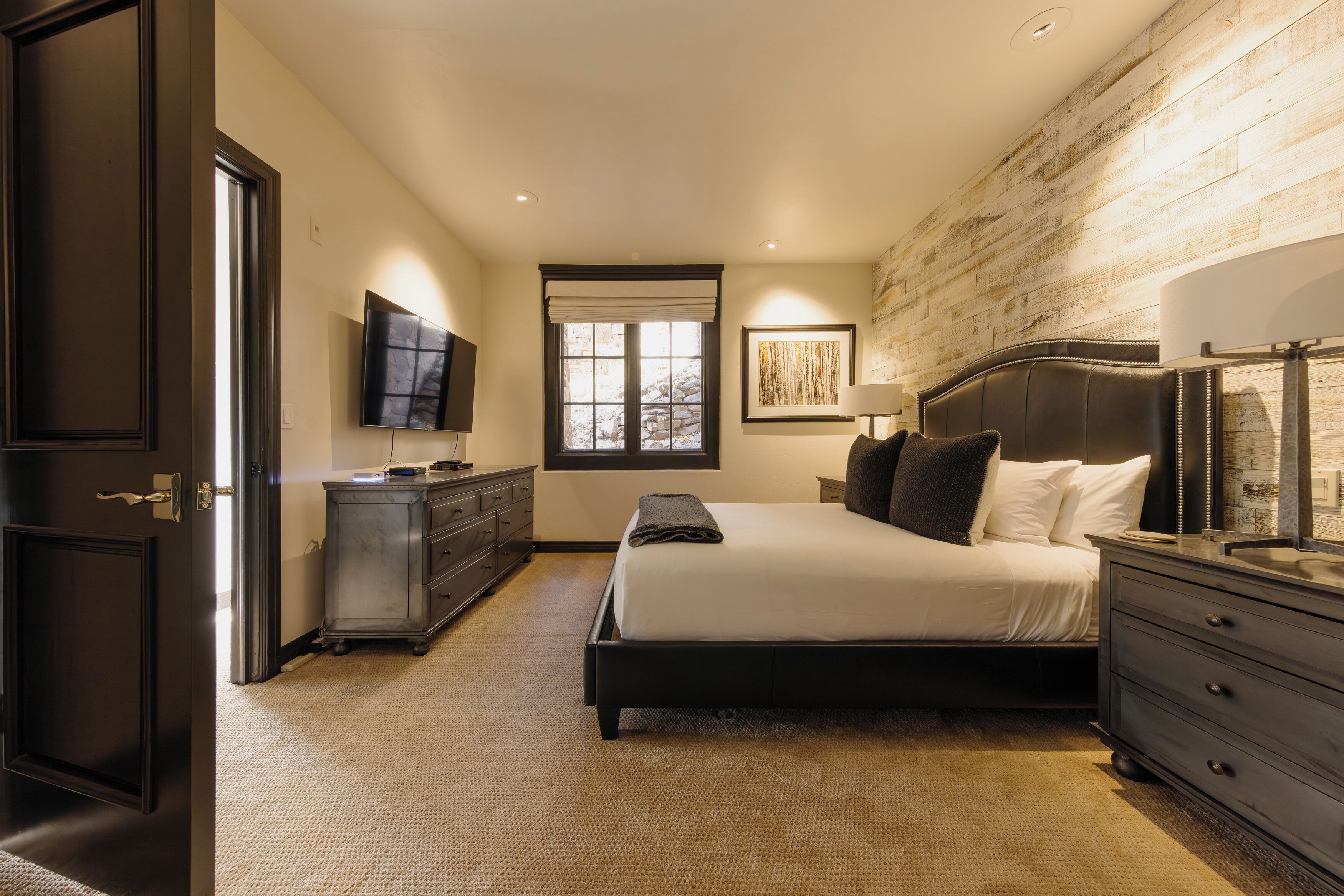 A bedroom with a bed, dresser, TV, and a window with a view.