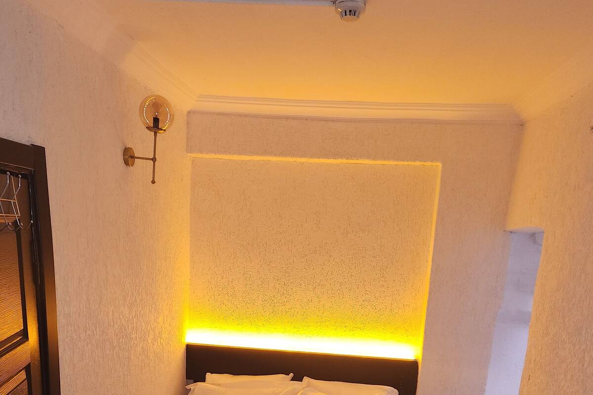 A neatly made bed with white linens and a folded towel, a bedside table, and a wall-mounted light fixture.
