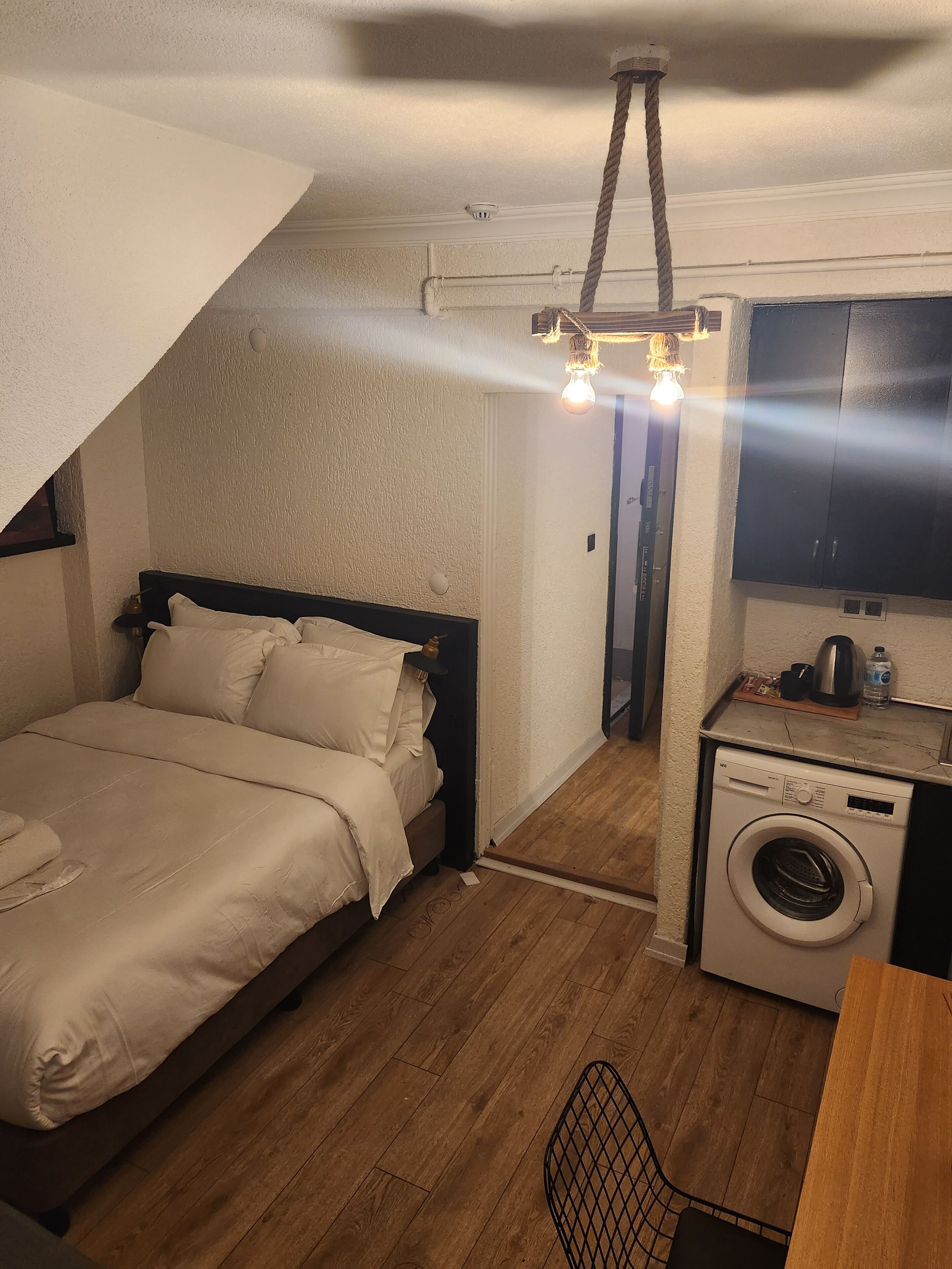 A compact bedroom with a bed, a washing machine, and a small kitchenette.