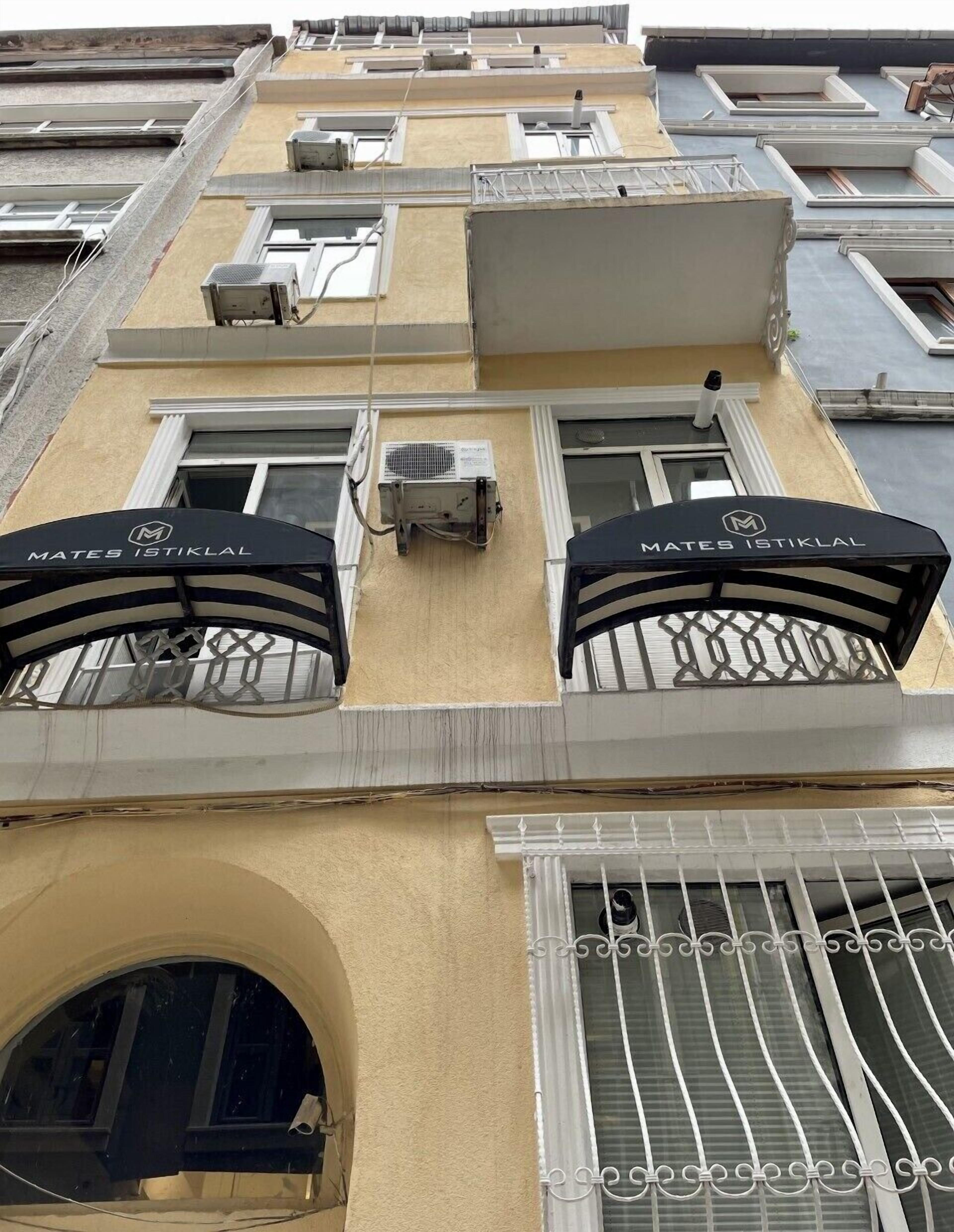 Een gevel met meerdere balkons, airconditionings en een opvallend 'MATES ISTIKLAL'-bord.