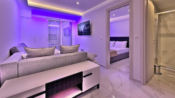 Quarto moderno com cama, sofá e um aparador para TV. Inclui banheiro com chuveiro e porta de vidro.