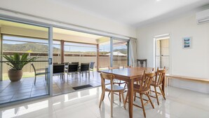 Il s’agit d’une pièce spacieuse dotée d’une grande porte-fenêtre coulissante qui donne sur un patio extérieur. À l’intérieur, on trouve une table à manger en bois, ainsi que des chaises et un banc.
