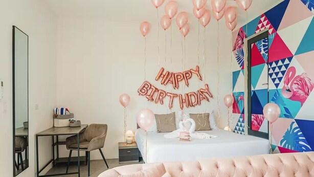 Une chambre avec un lit, un bureau et une chaise. On y voit des ballons et une pancarte avec l’inscription « Joyeux anniversaire ».