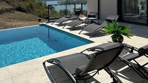 Ein moderner Poolbereich im Freien mit Liegestühlen und Blick auf einen See und Hügel.