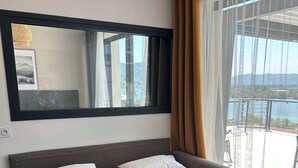 Ein Hotelzimmer mit einem großen Bett, einem Kopfteil, einem Fenster mit Vorhängen und Blick auf einen Balkon.