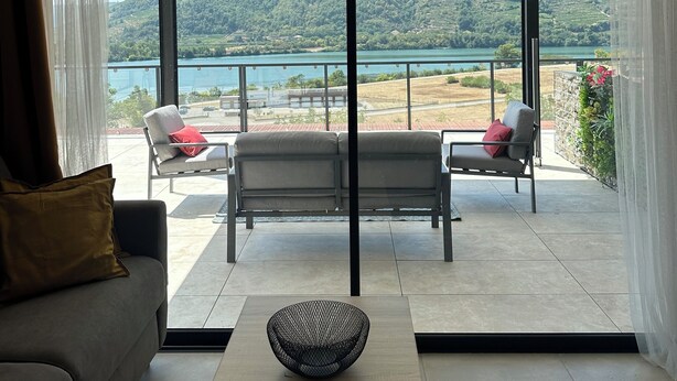 Ein modernes Wohnzimmer mit einer Couch, einem Couchtisch und Blick auf einen See und Hügel durch große Schiebeglastüren.