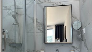 Ein modernes Badezimmer mit Duschkabine aus Glas, Marmorfliesen, einem weißen Waschtisch mit Spiegel und einem runden Wandspiegel.