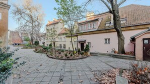 Une cour dallée de pierres, recouverte de feuilles, et bordée de bâtiments européens traditionnels aux toits de tuiles.