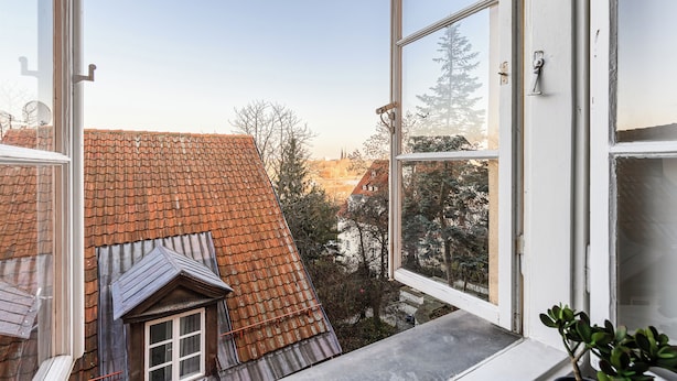 Une vue depuis une fenêtre donnant sur un bâtiment avec un toit recouvert de tuiles rouges et une petite fenêtre.