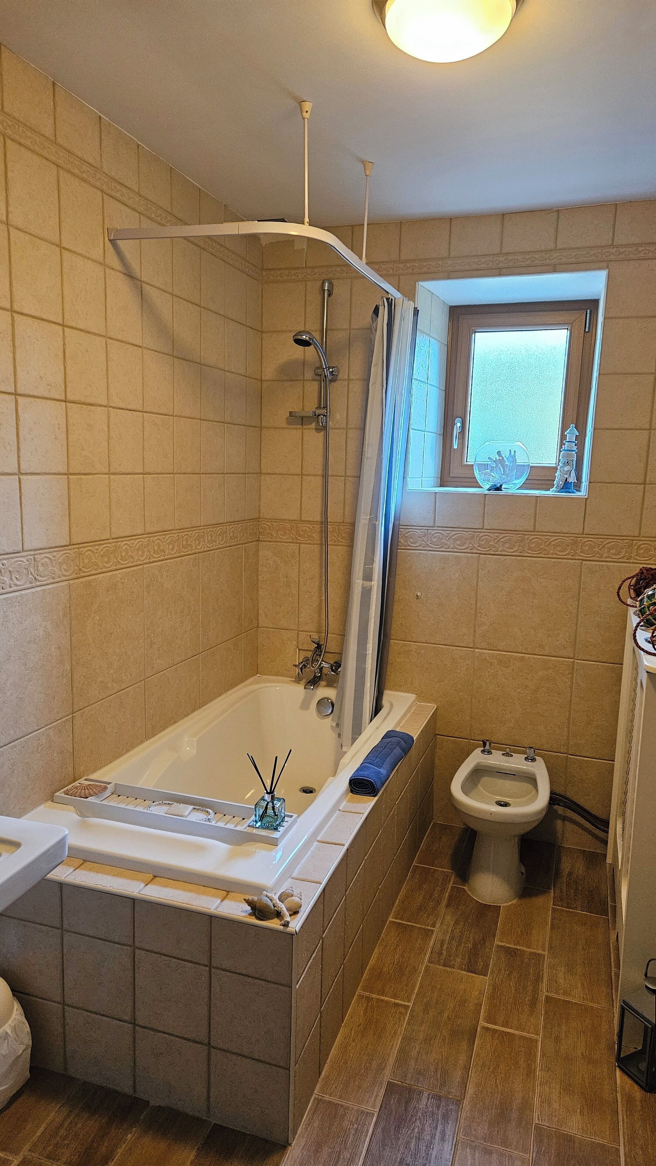 Een badkamer met een bad, douche, toilet en een raam.