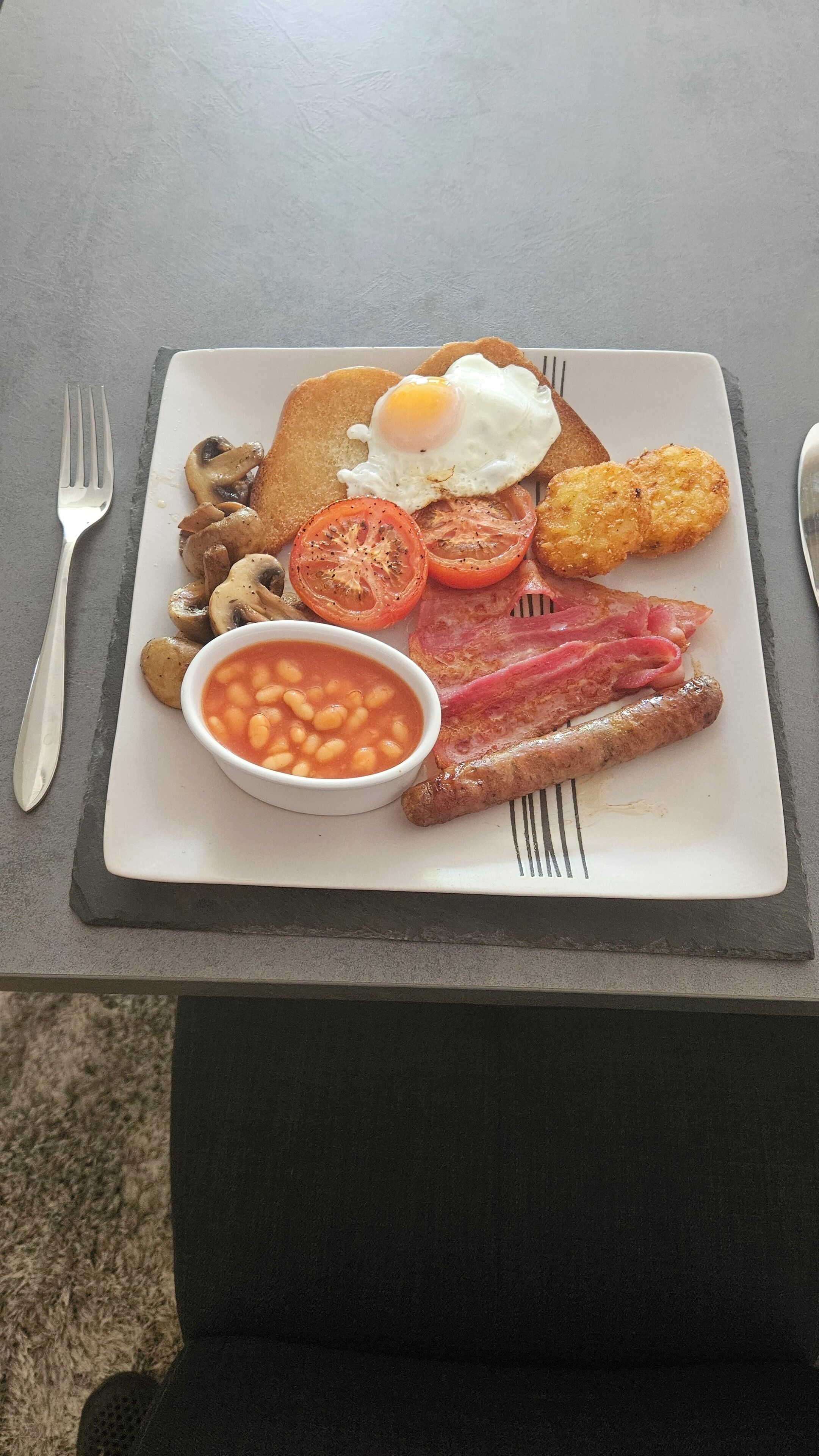 A plate of breakfast food including eggs, bacon, sausages, mushrooms, tomatoes, and beans.