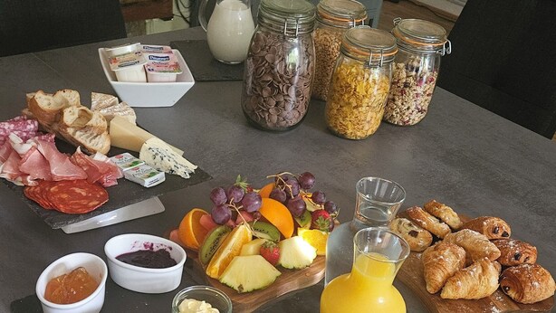 A breakfast table with various food items, including bread, cheese, fruits, and a glass of orange juice. - The Lions Den - La Loge Mantilly (Mantilly)