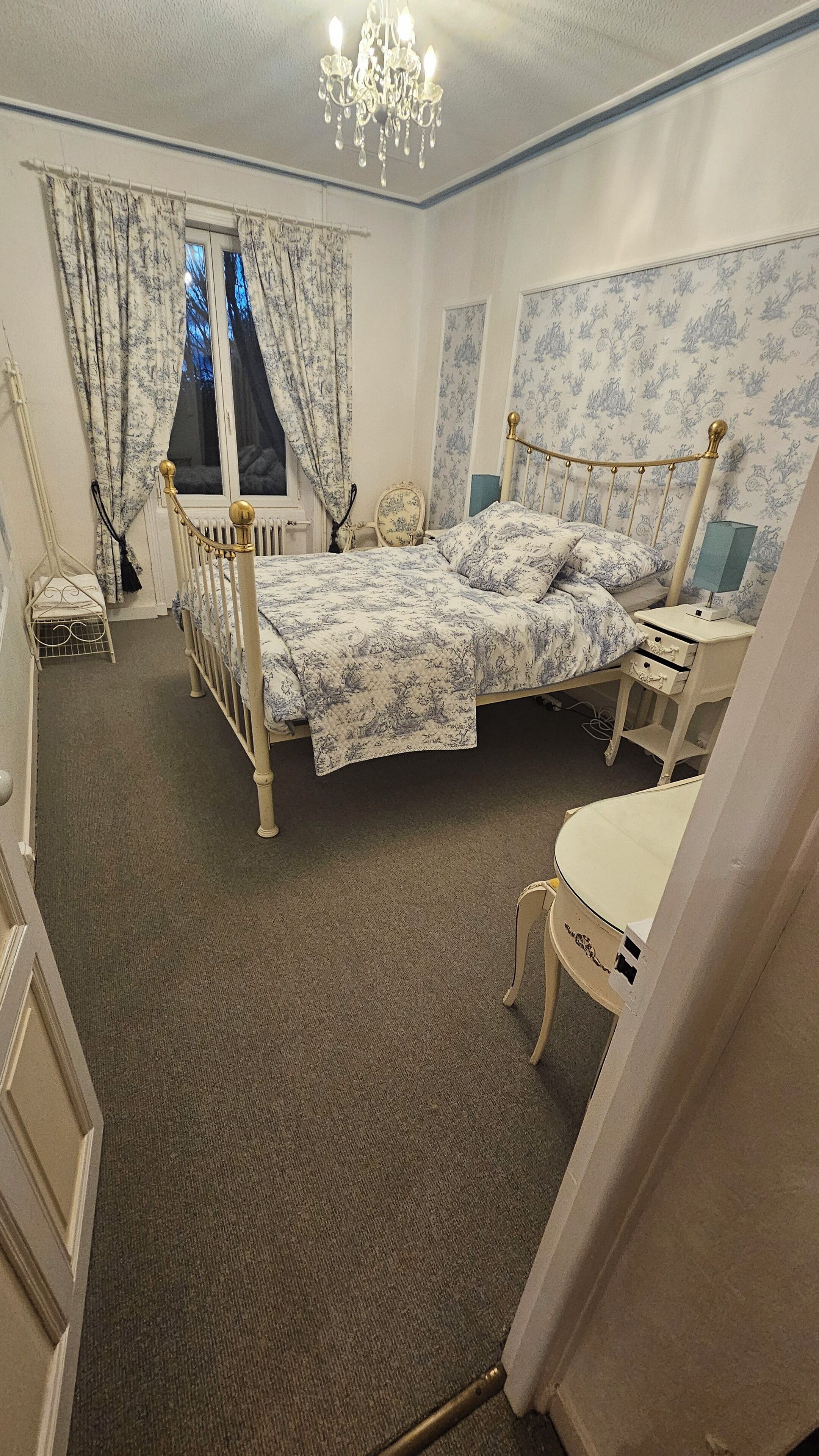A bedroom with a bed, a nightstand, a chair, a radiator, and a window with curtains.