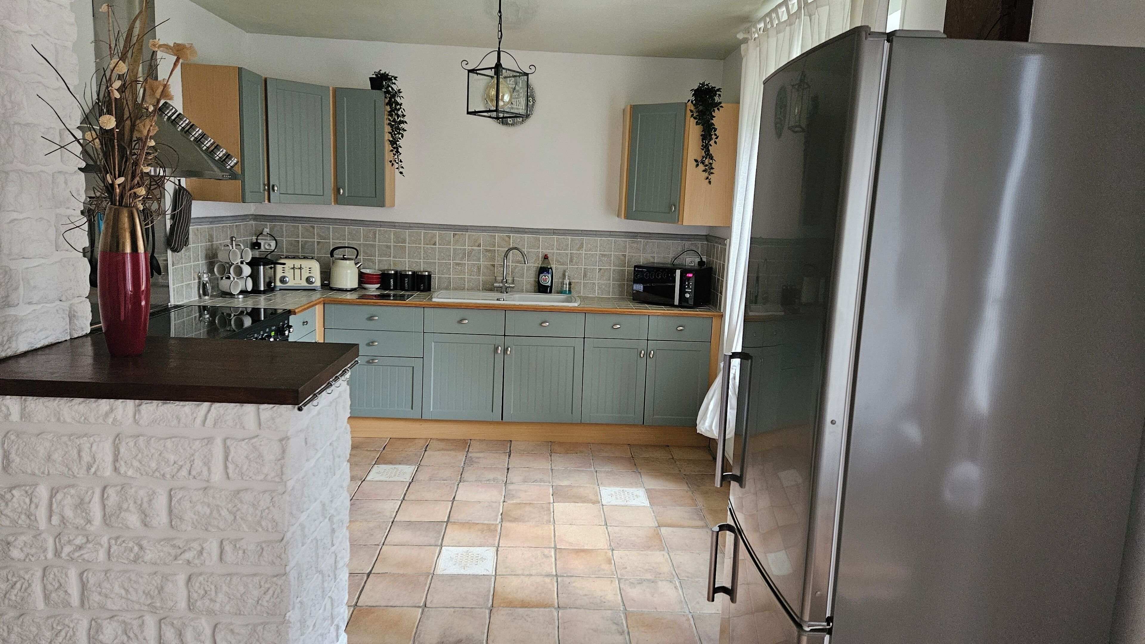 Una cocina con armarios azul claro, un refrigerador de acero inoxidable y salpicadero de azulejos.