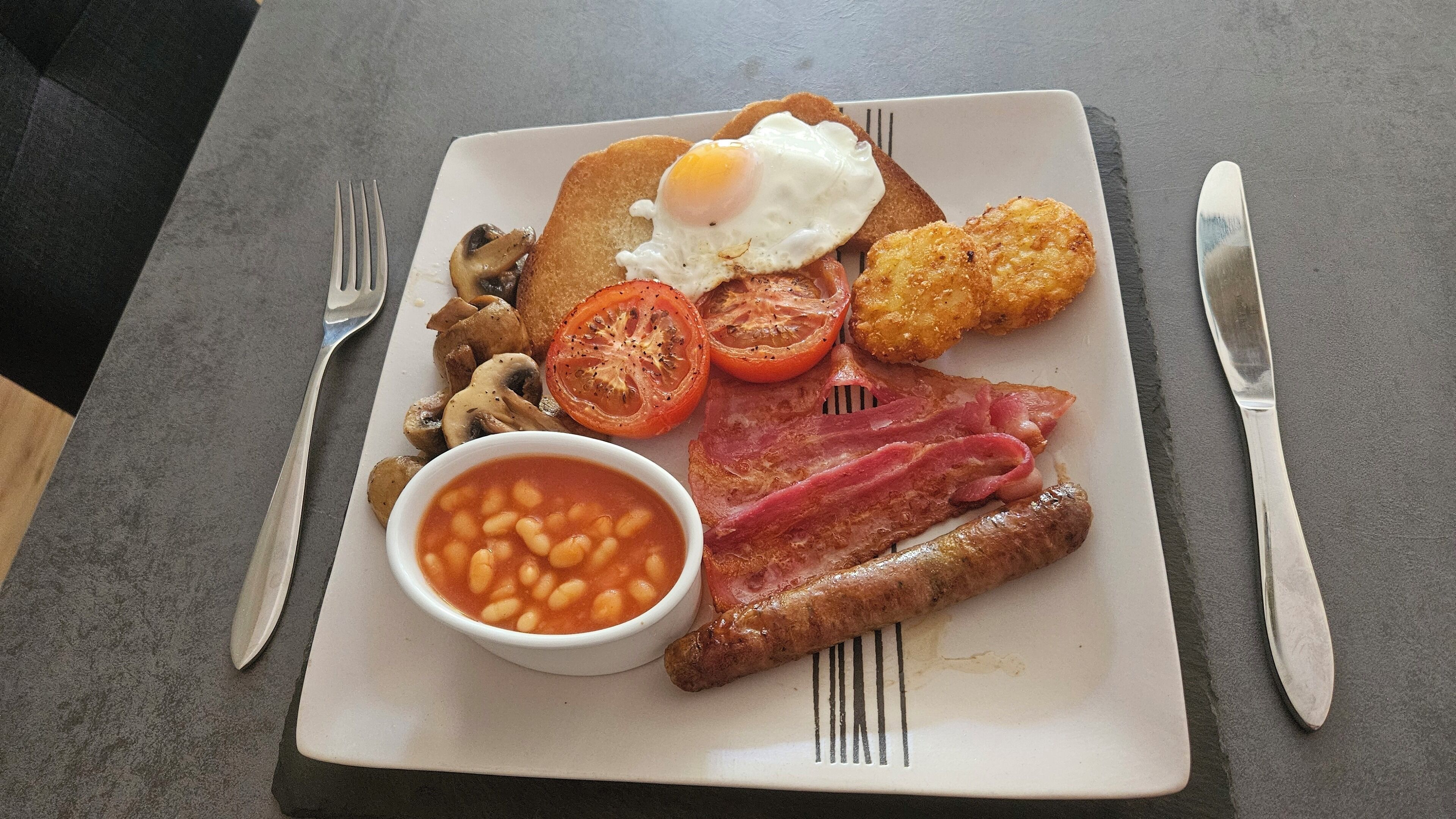 Une assiette de nourriture pour le petit-déjeuner comprenant des œufs, du bacon, des champignons, des tomates, des haricots et des saucisses.