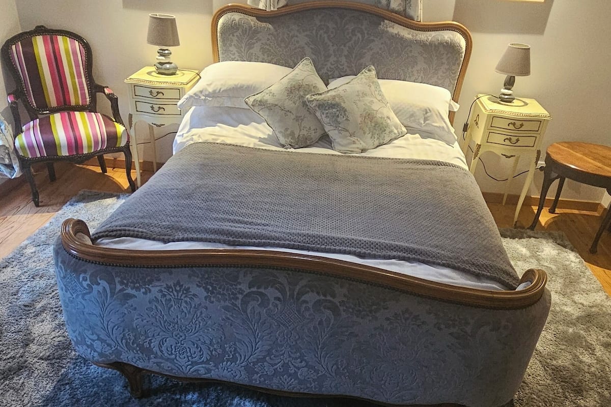 A bedroom with a large bed, a chair, a nightstand, and a window with curtains.