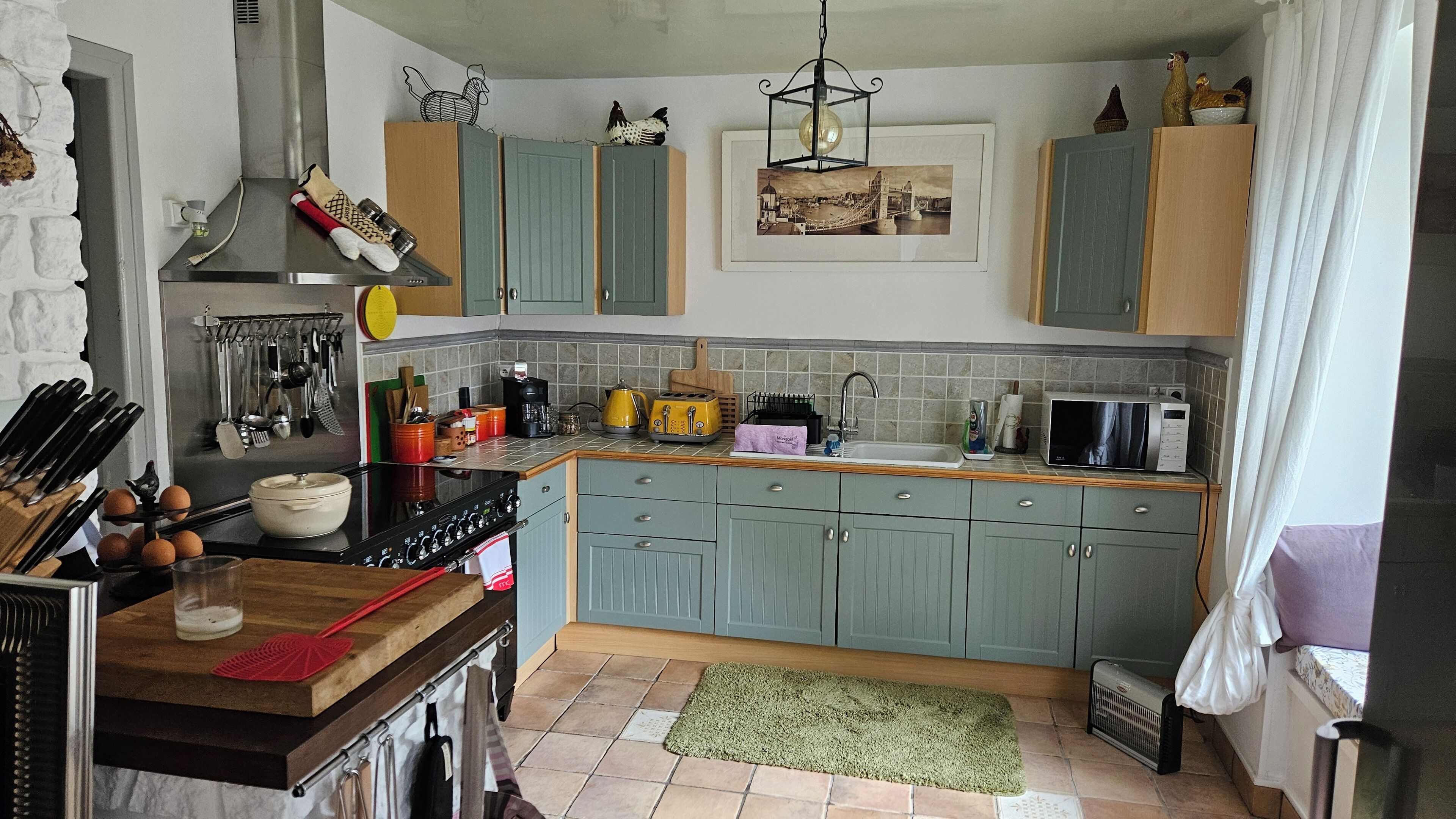 A kitchen with a stove, sink, and various appliances. There are cabinets, a window, and a rug on the floor.