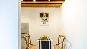 Un coin repas avec une table dressée pour deux personnes, agrémentée d’une nappe à rayures noires et blanches, de deux chaises en osier et d’une composition de fruits posée sur la table.