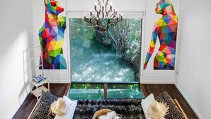 Une pièce dotée d’une grande fenêtre, d’un lustre, d’un tapis à motifs et de deux tables d’appoint ornées d’objets décoratifs.