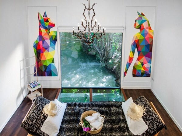 A room with a large window, a chandelier, a patterned rug, and two side tables with decorative items.