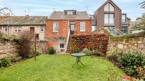 A residential backyard with a lawn, a small table, and a stone wall.