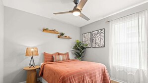 A bedroom with a bed, a ceiling fan, a bedside table with a lamp, a potted plant, and artwork on the wall. - The Cowgirl Cottage- Bright 3BR in The Nations + Close to Broadway & Dining (Nashville)