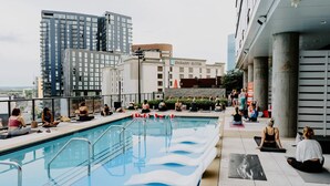 A rooftop pool area with people exercising, a building labeled 'EMBASSY SUITES,' and a cityscape in the background. - Kenect Nashville (Nashville)