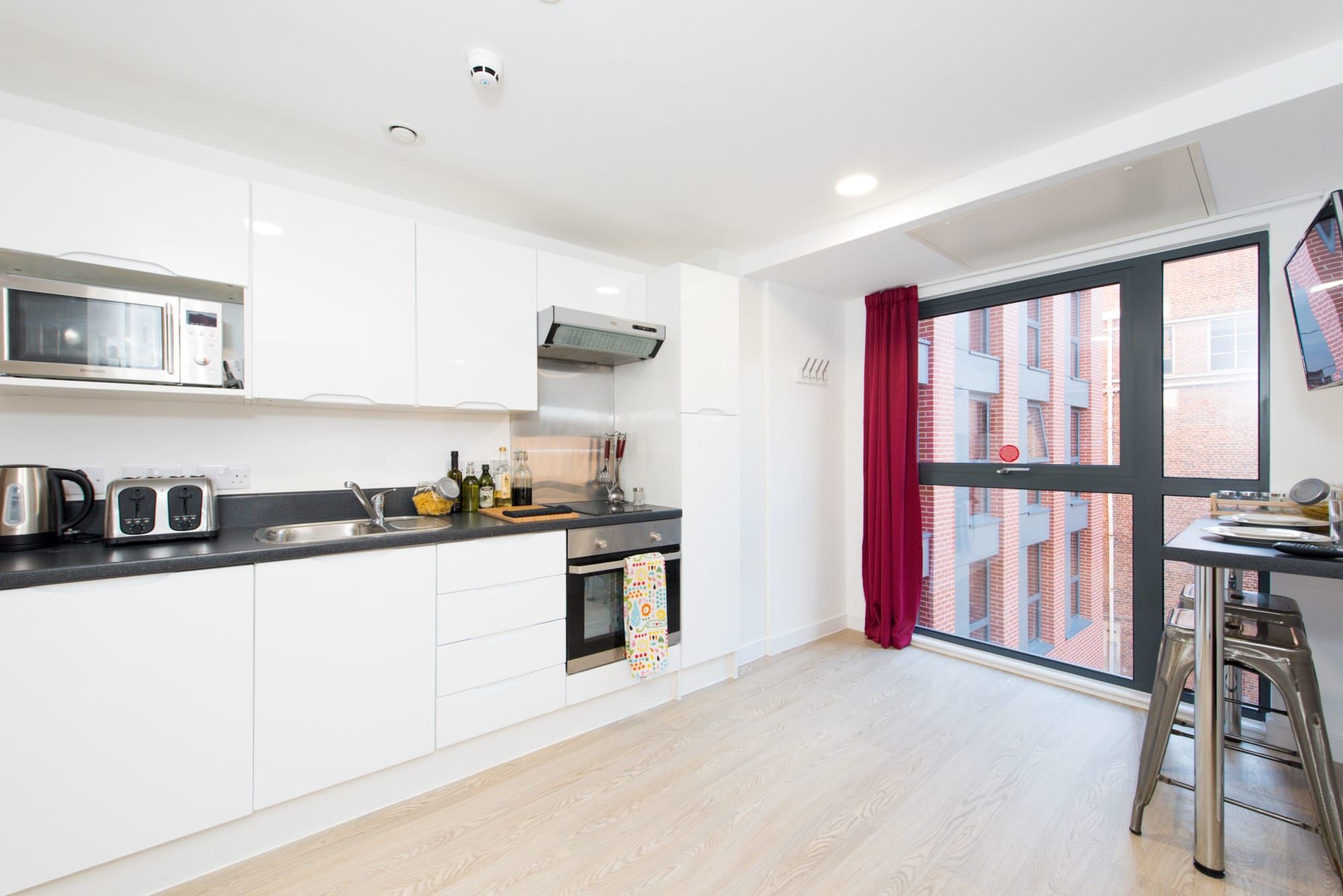 Eine moderne Küche mit weißen Schränken, einer Mikrowelle, einem Toaster und einem Fenster mit Blick auf ein Backsteingebäude.