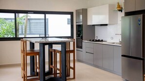Eine moderne Küche mit Esstisch und Stühlen, Edelstahlgeräten und einem großen Fenster mit Blick auf Grünflächen.