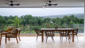 Ein Essbereich mit Tisch und Stühlen, einem Deckenventilator und Blick auf eine üppige Landschaft mit Bäumen und Hügeln.