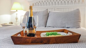 Ein Holztablett mit einer Flasche Ariel Brut Cuvée Champagner, zwei Gläsern und einer Platte mit Trauben auf einem Bett mit weißem Kopfteil und Kissen.
