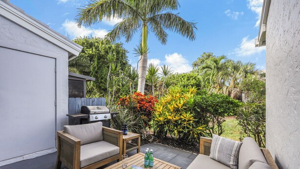 Eine Terrasse im Freien mit einem Holztisch, zwei Stühlen, einer Couch und einem Grill.