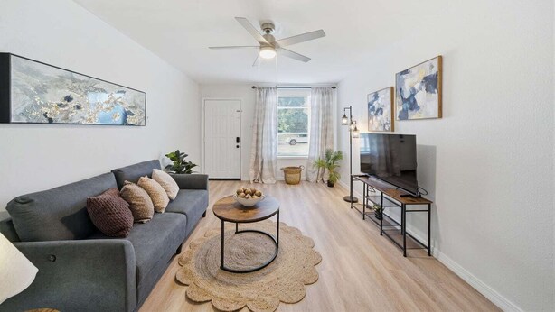 A modern living room with a grey sofa, a round coffee table, a ceiling fan, and a TV on a black stand. - Stay just minutes from Downtown in this cozy, well-designed 1-bedroom apartment. An ideal base for professionals, students, and travelers wanting fast access to Houston’s best dining and attractions. (Houston)