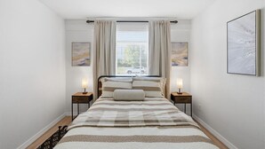 A bedroom with a bed, two bedside tables, a window with curtains, and two wall-mounted artworks. - Stay just minutes from Downtown in this cozy, well-designed 1-bedroom apartment. An ideal base for professionals, students, and travelers wanting fast access to Houston’s best dining and attractions. (Houston)