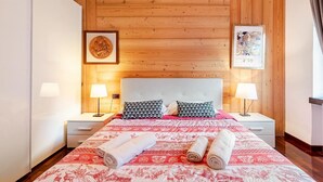 Une chambre avec un plafond en bois, un grand lit avec une literie à motifs, deux lampes de chevet et deux serviettes enroulées posées sur le lit.