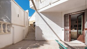 A courtyard with a staircase leading to a second floor, a door with a wooden frame, and a tiled floor. - Casa Paola (Alezio)