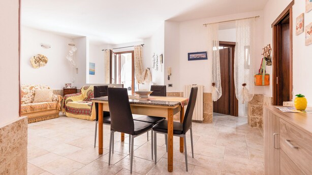 A dining area with a wooden table and chairs, a sofa, and a kitchen area with cabinets and a countertop. - Casa Paola (Alezio)