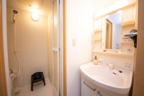 A bathroom with a shower, a sink, a mirror, and a small stool. - goom Hotel Nakasu Bluge (Fukuoka)